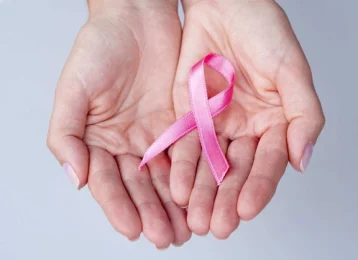 Mão feminina segurando delicadamente um laço rosa em um ambiente acolhedor, simbolizando a campanha do Outubro Rosa e a importância do diagnóstico precoce do câncer de mama.