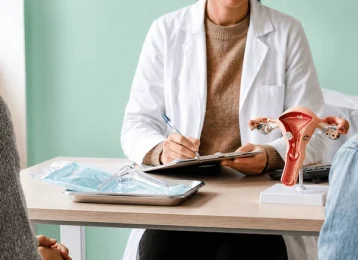 Médica ginecologista orientando mãe e filha jovem em consulta acolhedora com modelo anatômico do útero, explicando quando levar sua filha ao ginecologista.